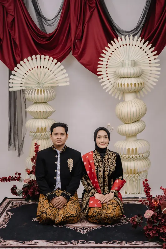 Kedua mempelai duduk berdampingan mengenakan busana Jawa